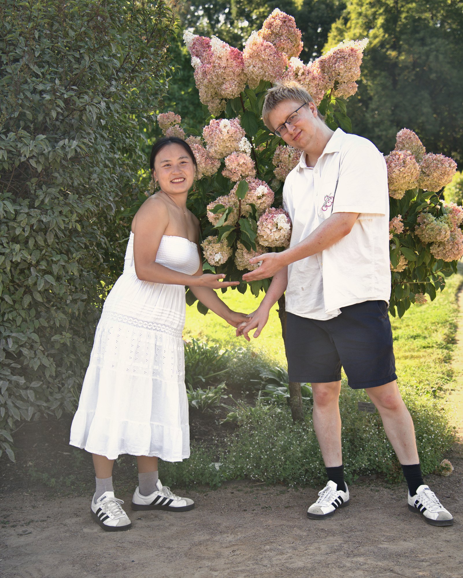 Playful couple making a heart with their hands in front of pink hydrangeas — Twin Cities couples and engagement photography by Loon & Birch Photography