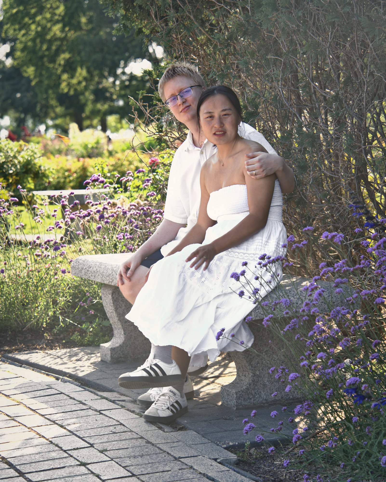 Couple sitting close on a stone bench surrounded by purple verbena — Twin Cities couples and engagement photography by Loon & Birch Photography