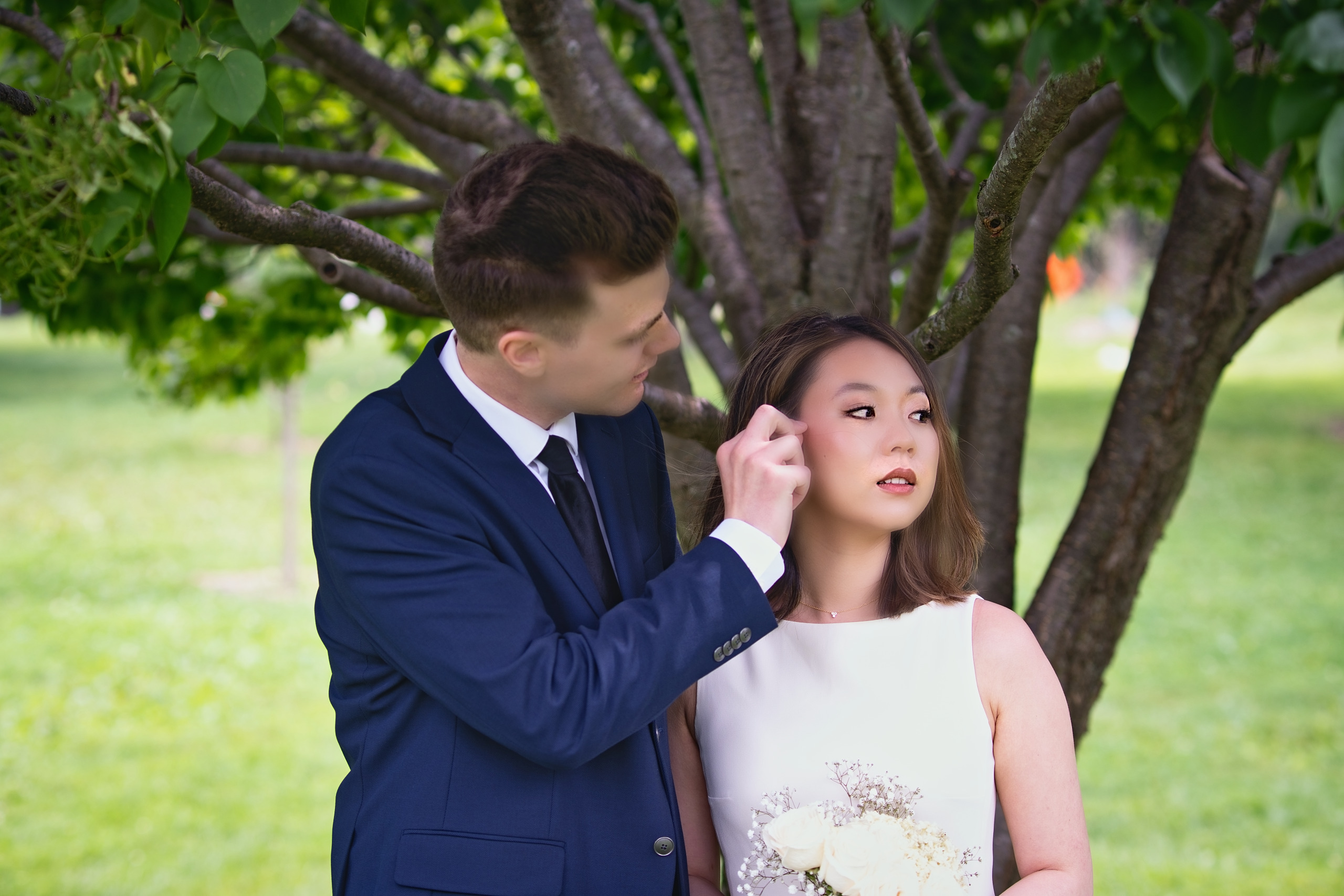 Groom tucking a strand of hair behind the bride under a spring tree — Twin Cities wedding photography by Loon & Birch Photography