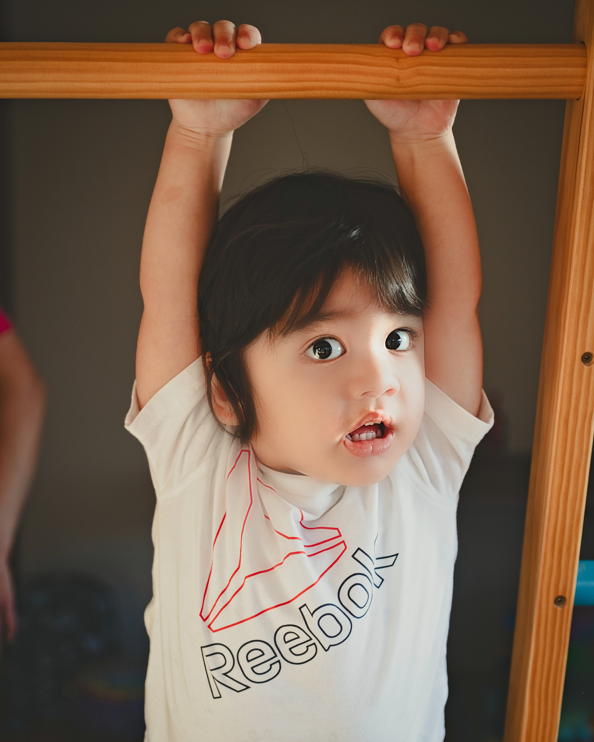 Toddler hanging from a doorway bar with a curious expression — Twin Cities family photography by Loon & Birch Photography