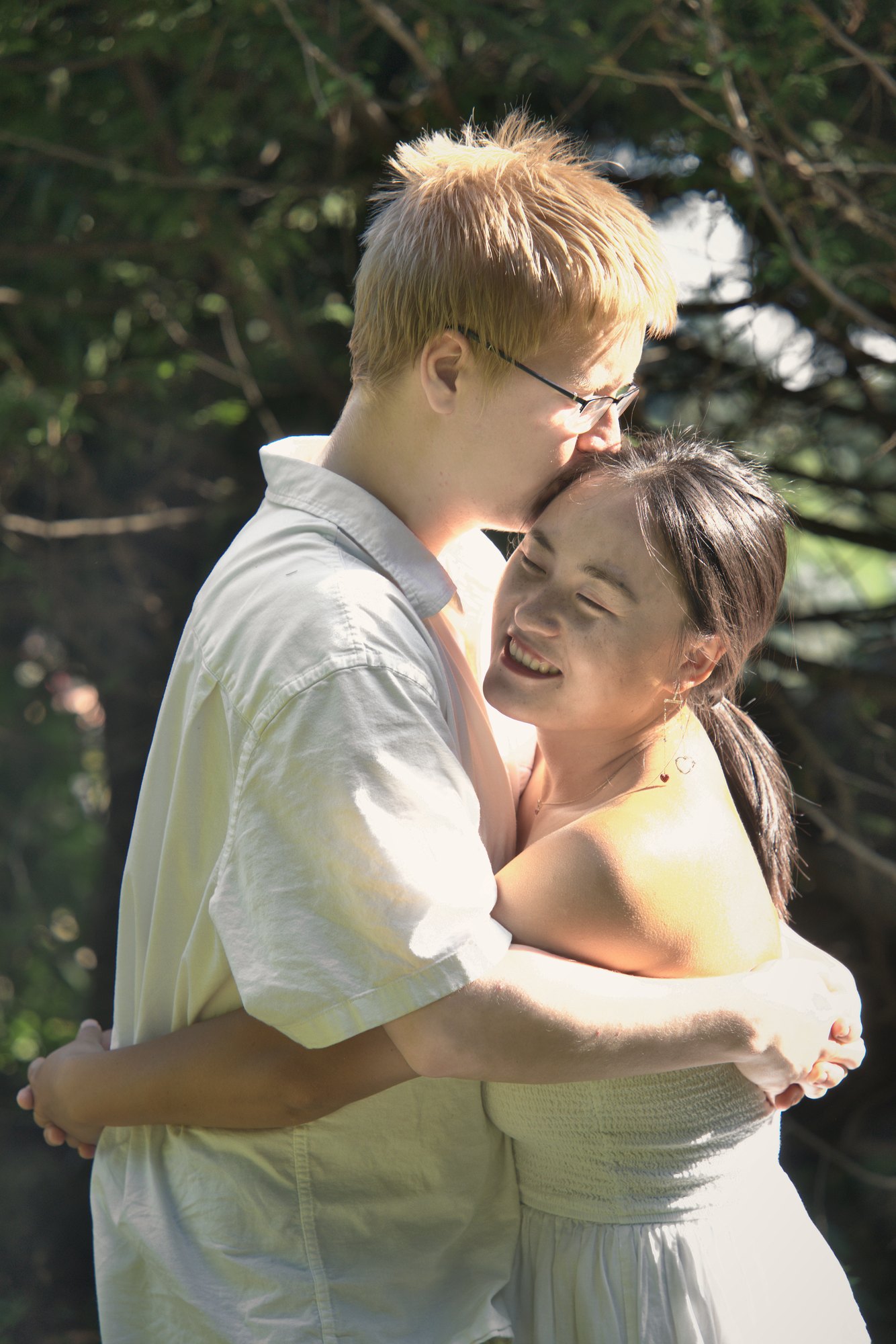 Man kissing his partner's forehead in a sunlit embrace among evergreens — Twin Cities couples and engagement photography by Loon & Birch Photography